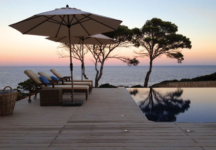 Terrasse und Poolumrandung mit WPC Terrassendielen und Sonnenschirmen bei Sonnenuntergang mit Meerblick