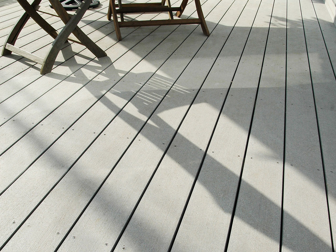 Hellgrauer Bodenbelag auf Balkon im Sonneschein mit Schattenwurf von Gartenmöbeln (Detailausschnitt)