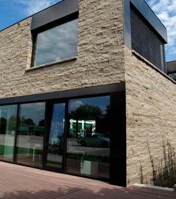 Modernes Natursteinhaus mit viel Glas und wetterfester Terrasse aus WPC Dielen