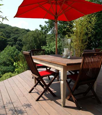 Dielen aus WPC in dunkelbraun auf Terrasse mi Gartentisch und rotem Sonnenschirm