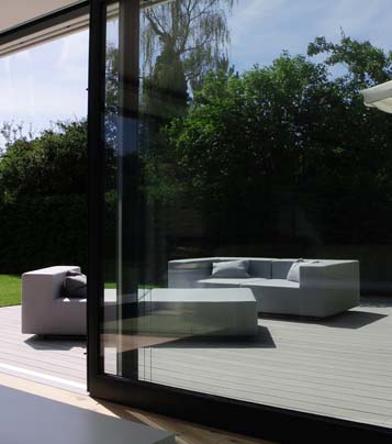 Blick auf moderne WPC Terrasse mit modernen Gartenmöbeln durch gläserne Schiebetür