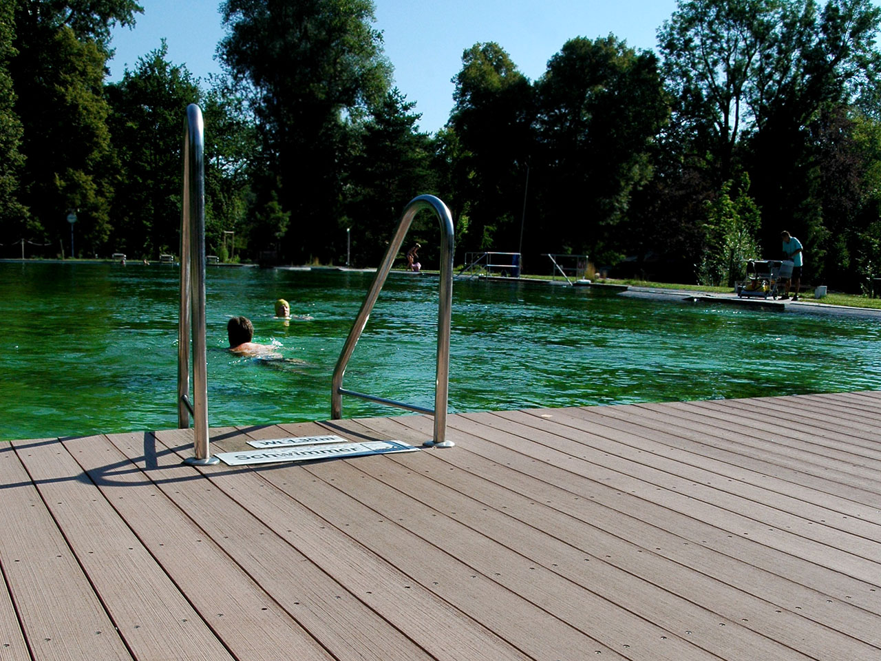 Rutschfeste WPC Poolumrandung in Schwimmbad mit Wasserleiter und Pool im Hintergrund