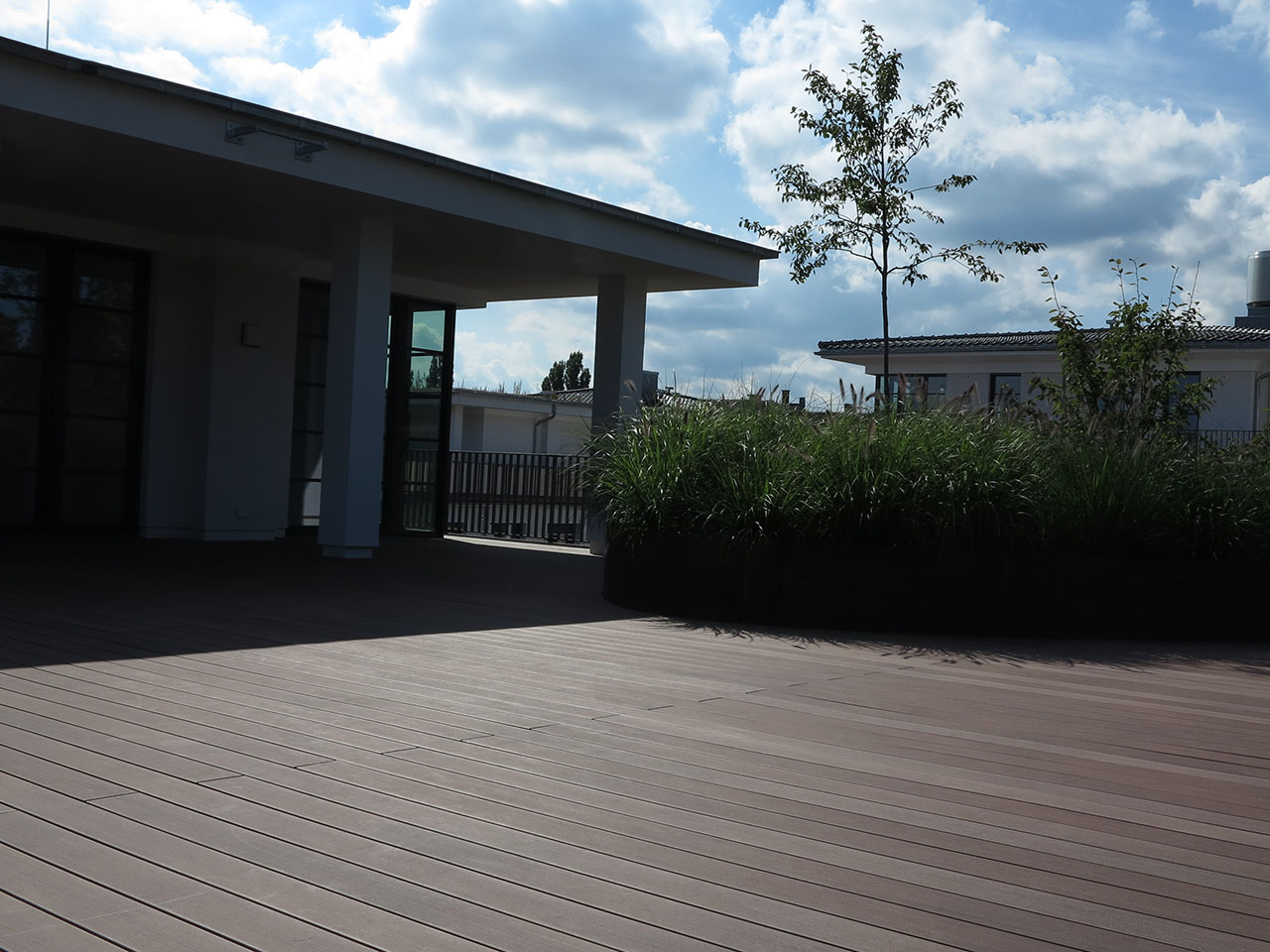 Braune Balkonhölzer aus WPC auf Penthouseterrasse mit Haus im Hintergund