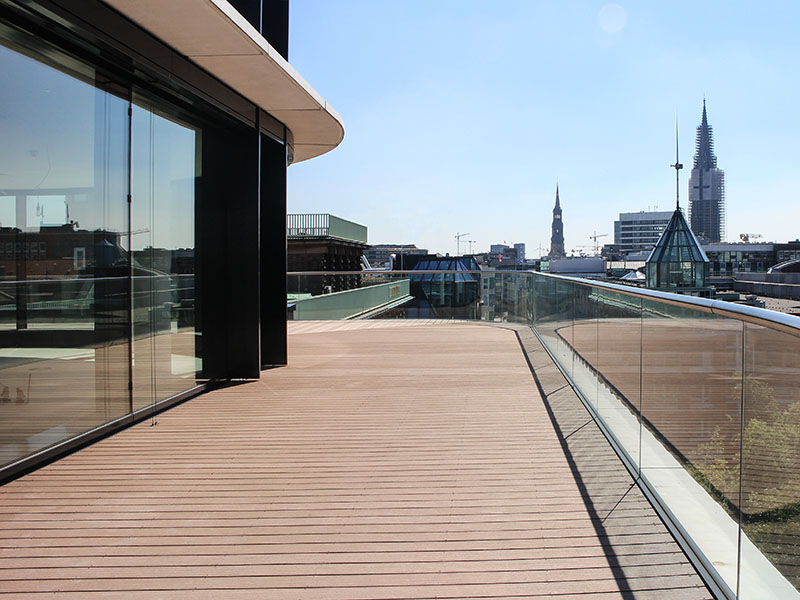 Hellbrauner Terrassenbelag auf geschwungener Terrasse mit Glasgeländer