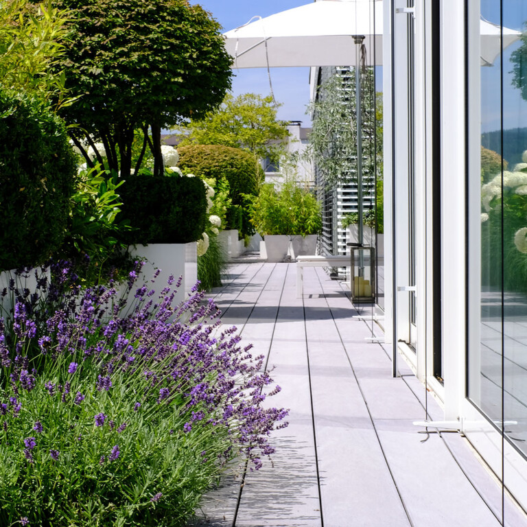 Grauer WPC Terrassenbelag auf Terrasse mit großzügiger Bepflanzung