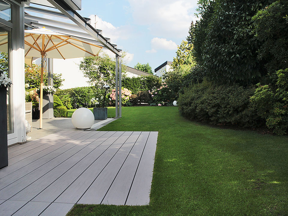 Gemütliche Terrasse mit WPC Dielen bei Sonnenschein mit aufgespanntem Sonnenschirm und gepflegter Garten