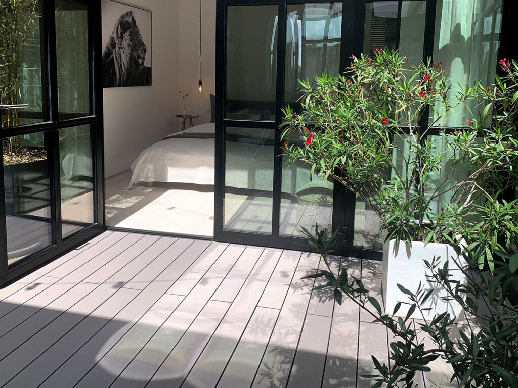 Blick von Terrasse mit grauen Holzoptik Dielen in den Schlafbereich des modernen Lofts mit Industrie-Sprossenfenstern