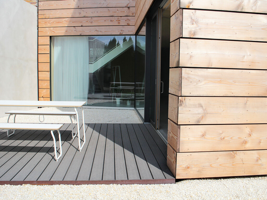 Abschlussleiste der WPC Terrasse aus rostendem Stahl. Moderner Kontrast aus Holz an der Fassade, WPC auf der Terrasse und weißem Kies auf der Bodenfläche.