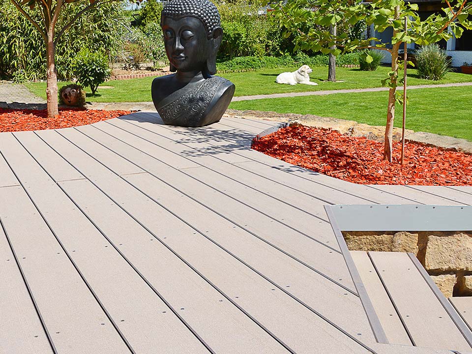 Graue WPC Gartenterrasse mit asiatischen Dekoelementen und rotem Rindenmulch um die Bäume herum