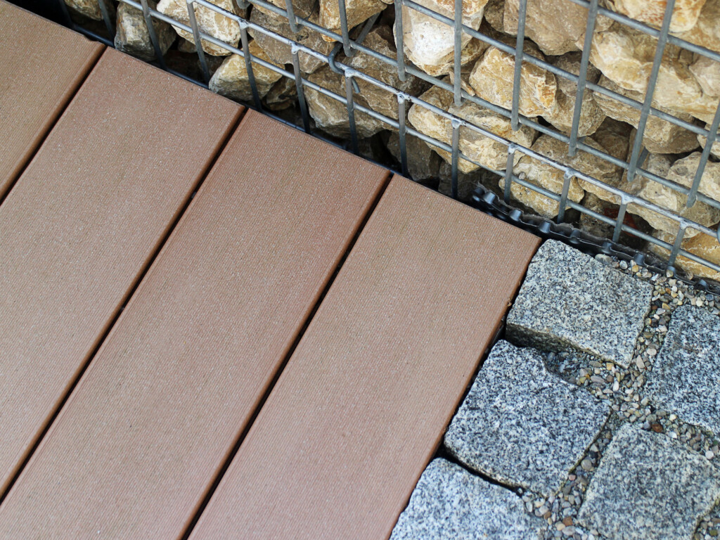 Kombination von zweierlei Steinen und braunen WPC Dielen als Übergang der Terrasse