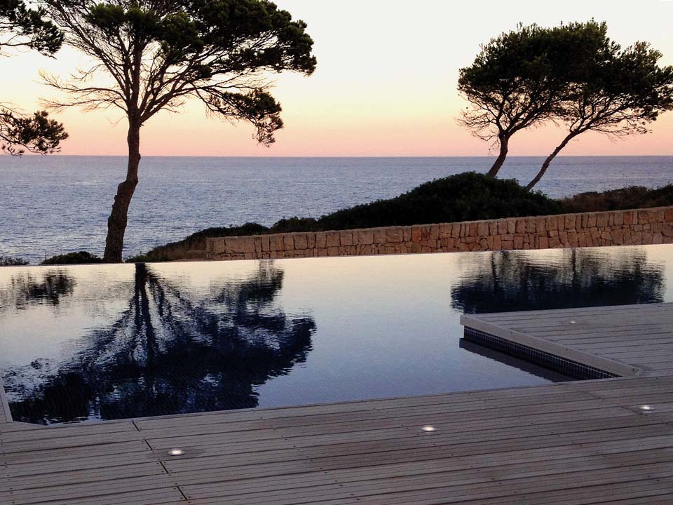 An Pool angrenzende WPC Terrasse mit eingelassenen Lichtern bei Abendstimmung mit Blick aufs Meer.