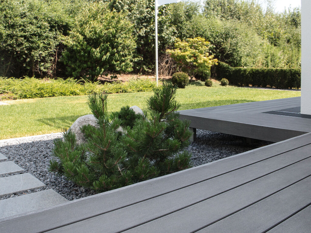 Die dunkelgraue WPC Terrasse scheint zu schweben und gibt Blick in minimalistischen Garten frei