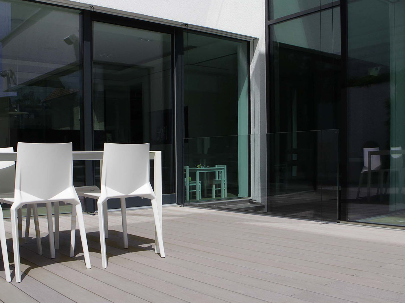 Die steingrauen WPC Terrassendielen fügen sich ideal in das Ambiente der modernen Terrasse mit viel Glas an der Hausfassade ein.