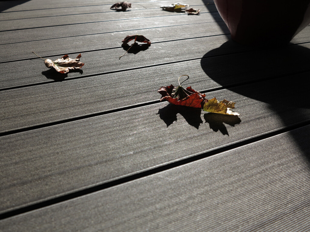 Fein strukturierte Oberfläche der WPC Dielen auf denen Herbstlaub liegt.