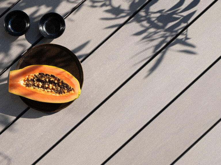 Größe für Mobile Version: Graue WPC Terrassendielen mit glattem Design auf Terrasse mit Schatten von Baum.