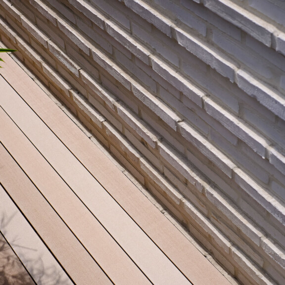 MYDECK WPC Massivdielen in hellen Brauntönen auf Terrasse mit angrenzendem Backsteingebäude