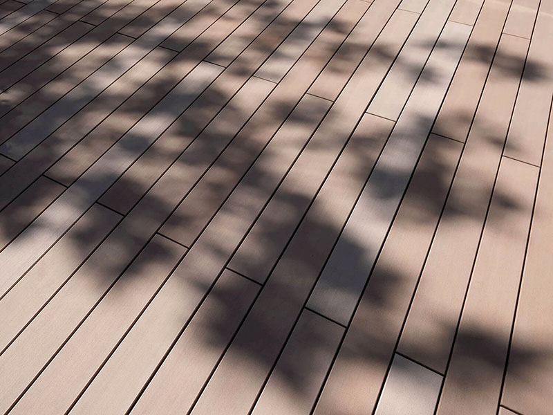 Verlegemuster glatte helle WPC Terrassendielen auf Terrasse mit Schafften von Bepflanzung