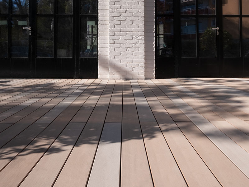 Terrasse mit hellen WPC Terrassendielen in Sandtönen von hellbraun, bis hellgrau vor Backsteingebäude