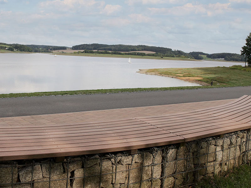 Bank mit Sitzfläche aus braunen WPC Dielen und Blick auf See