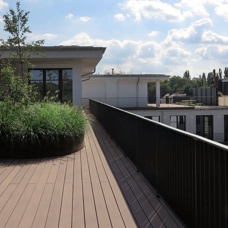 Terrasse mit braunen WPC Dielen und rundem Hochbeet bepflanzt mit Gräsern