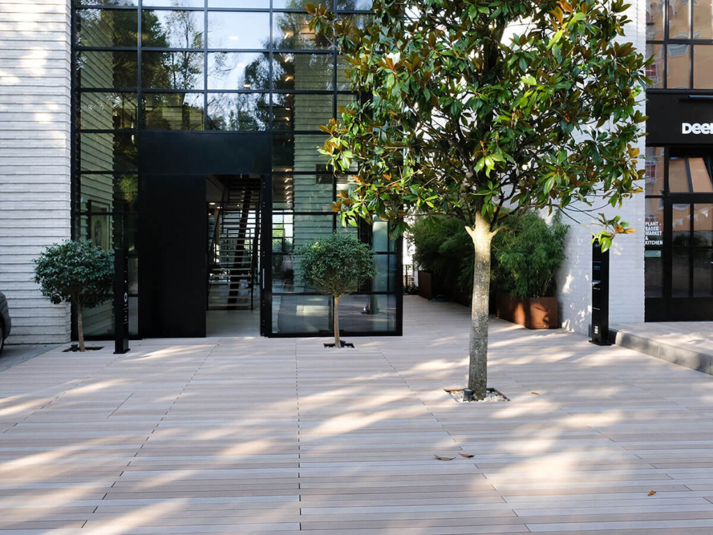 Erdverbundene Beete mit Magnolienbaum und anderen Bäumen auf Terrasse mit WPC Dielen vor Haus mit Loft-Fassade