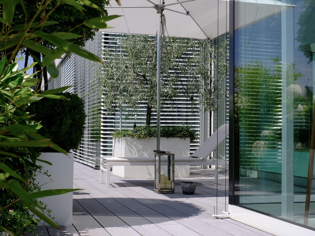 Terrassenbelag glatt grau mit weißen Hochbeet mit Bepflanzung Baum, Sitzplatz