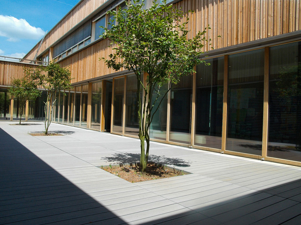 WPC Terrassendielen grau in Atrium mit Bäumen und Holzfassade