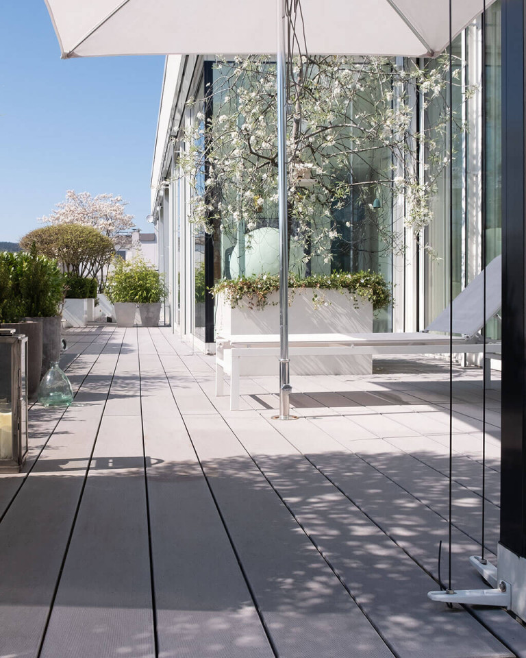 Moderne Designterrasse mit grauen breiten WPC Terrassenbelag und Sonnenliege