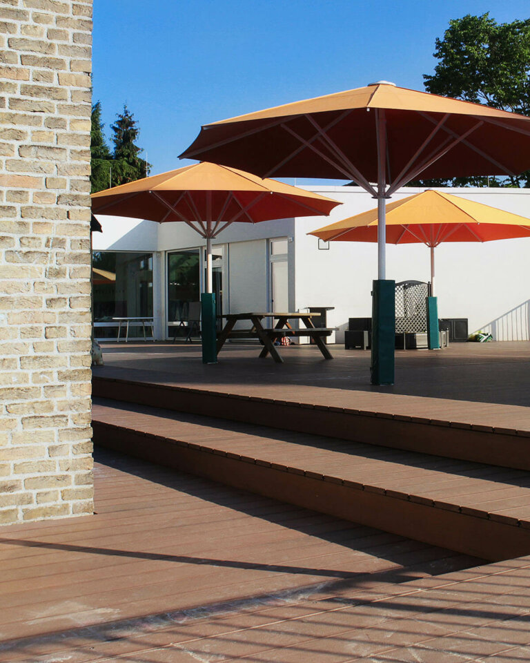 Stufenförmige Terrasse in Kita mit Premium WPC Massivdielen und großen roten Schirmen